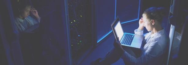 Una mujer en un cuarto oscuro mirando el monitor de un ordenador portátil para informarse de las medidas para mitigar los incidentes de ciberseguridad.